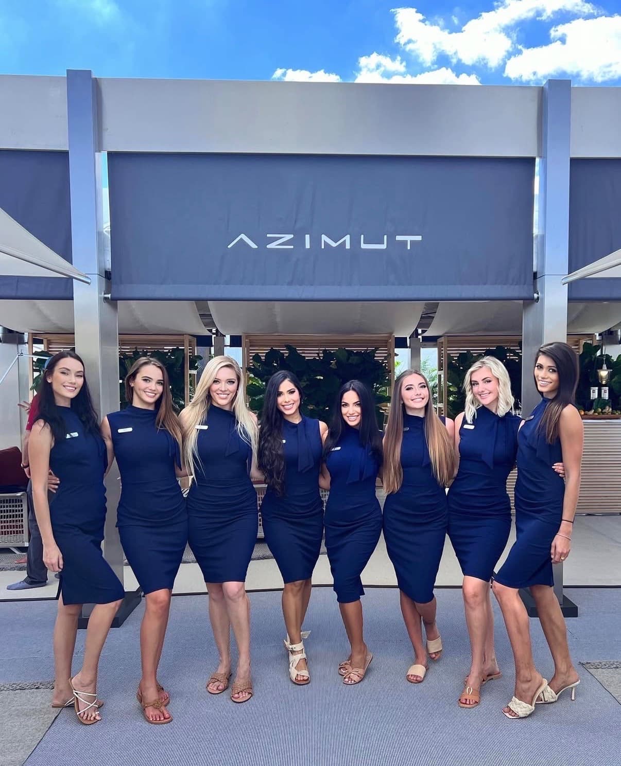 Eight brand ambassadors in matching navy dresses pose in front of an Azimut Yachts dealer sign at a dockside boat show.