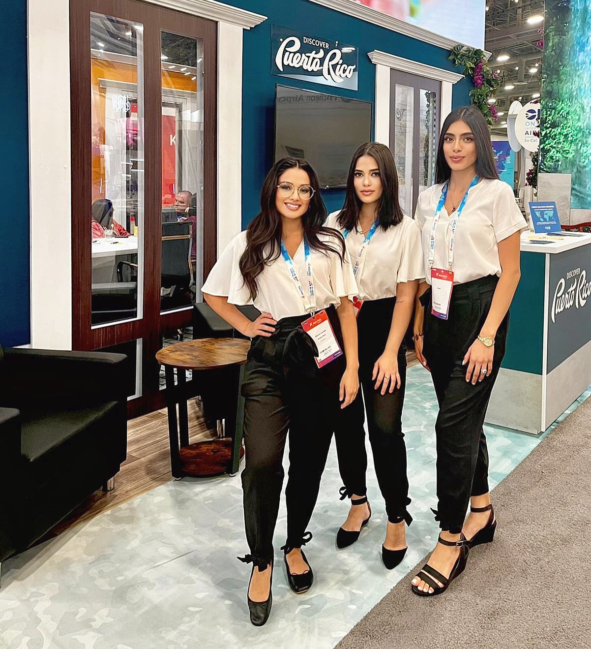 Three brand ambassadors in white blouses and black trousers with event badges staff a Discover Puerto Rico trade show booth.