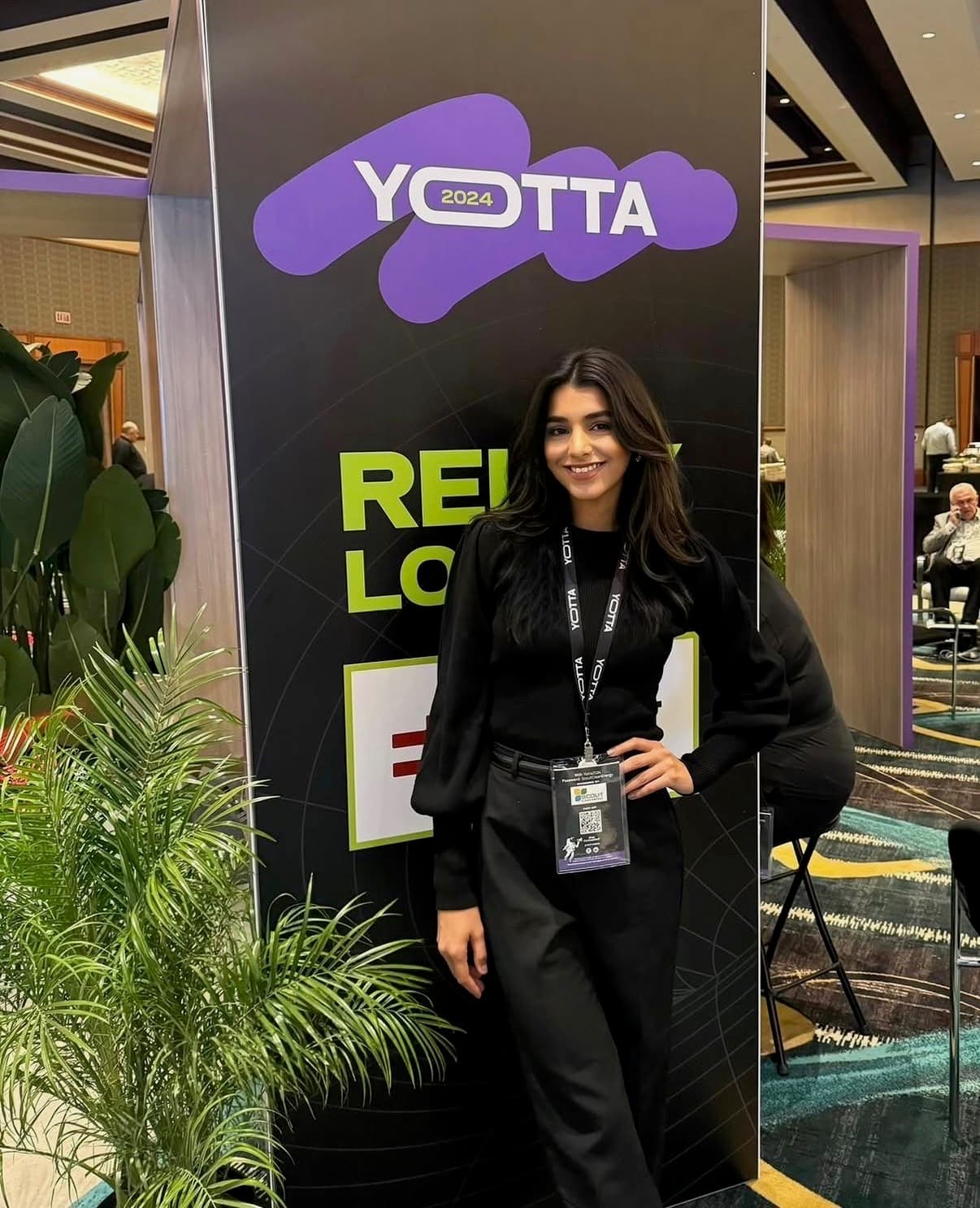 A brand ambassador in professional black attire with an event badge poses at the Yotta 2024 conference.